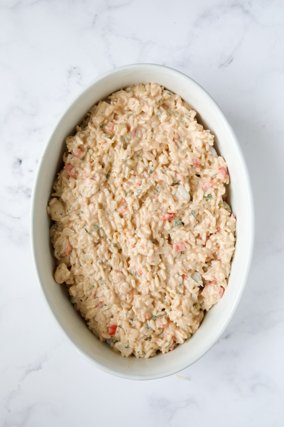 Layer of rice over the seafood in white oval baking dish.