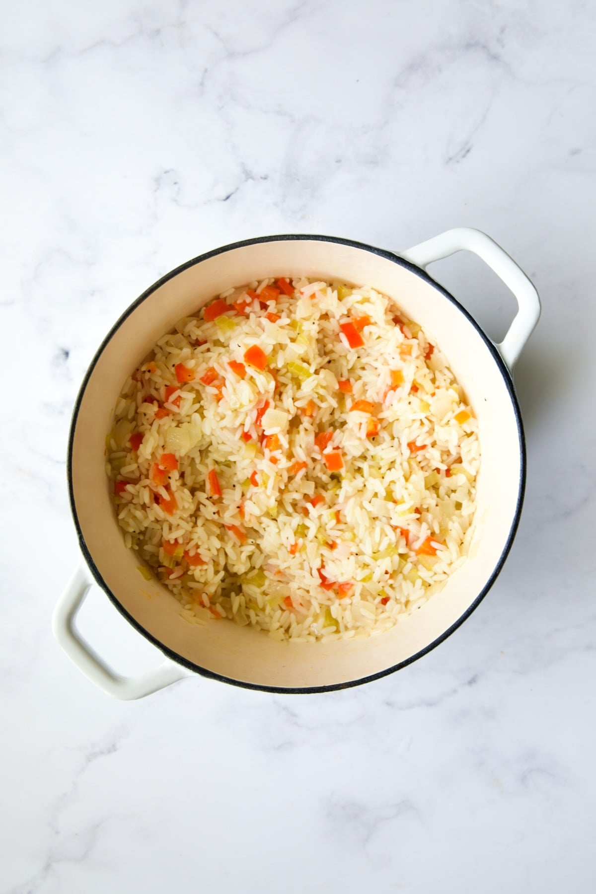 Cooked white rice with vegetables in white Dutch oven.