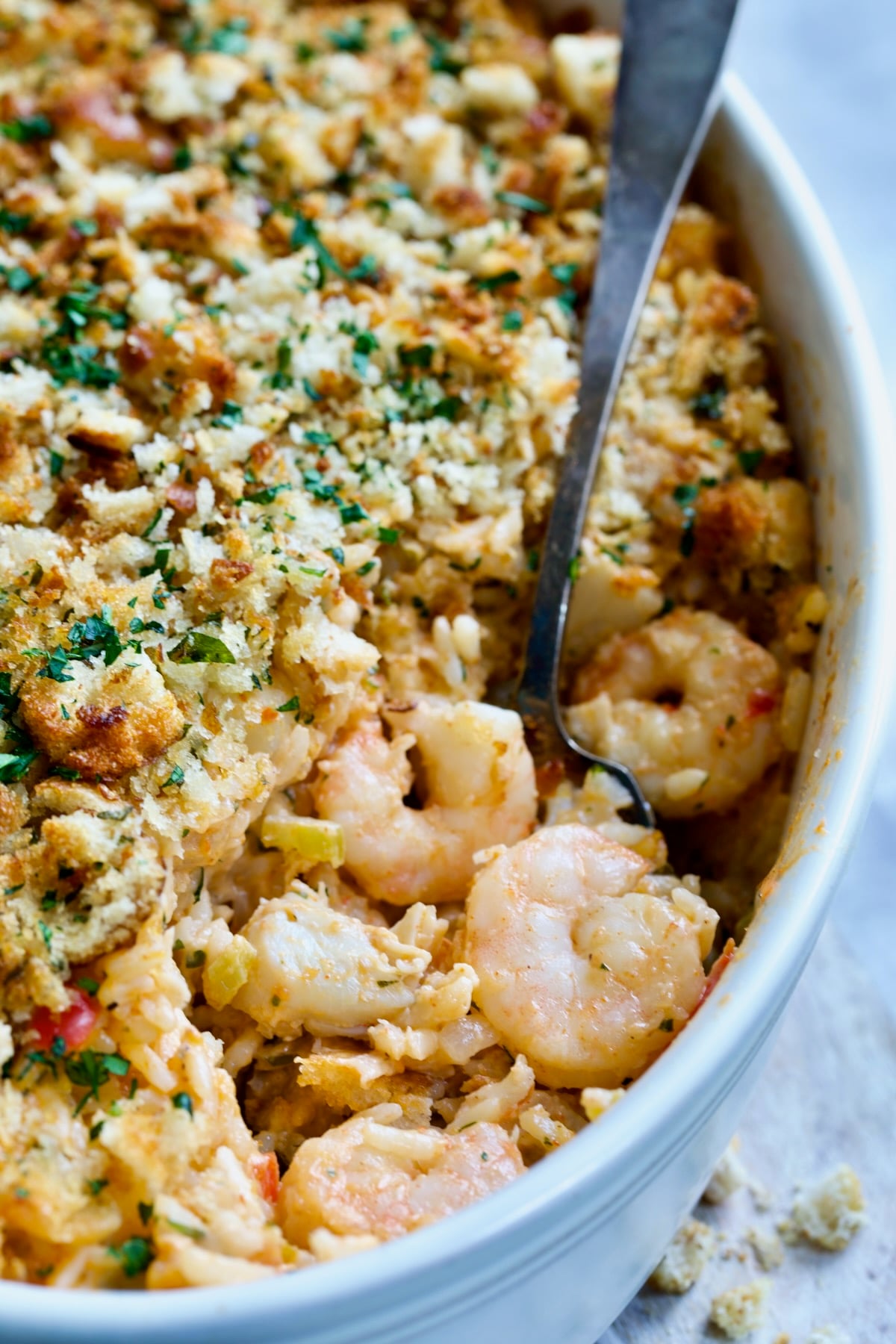 Shrimp and Crab Seafood Casserole in white baking dish with serving spoon scooping up shrimp and crab.