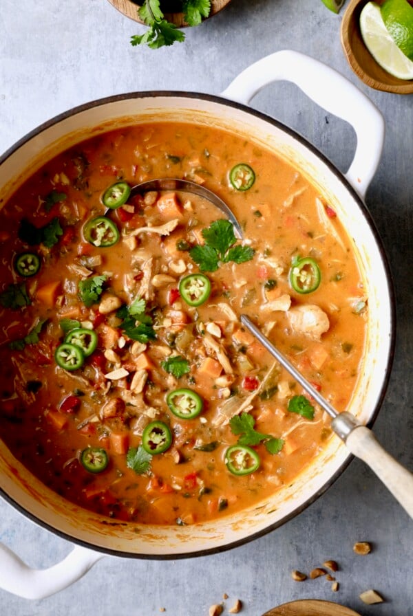 Spicy Chicken, Sweet Potato and Peanut Soup garnished with cilantro and jalapeno slices in white Dutch oven.