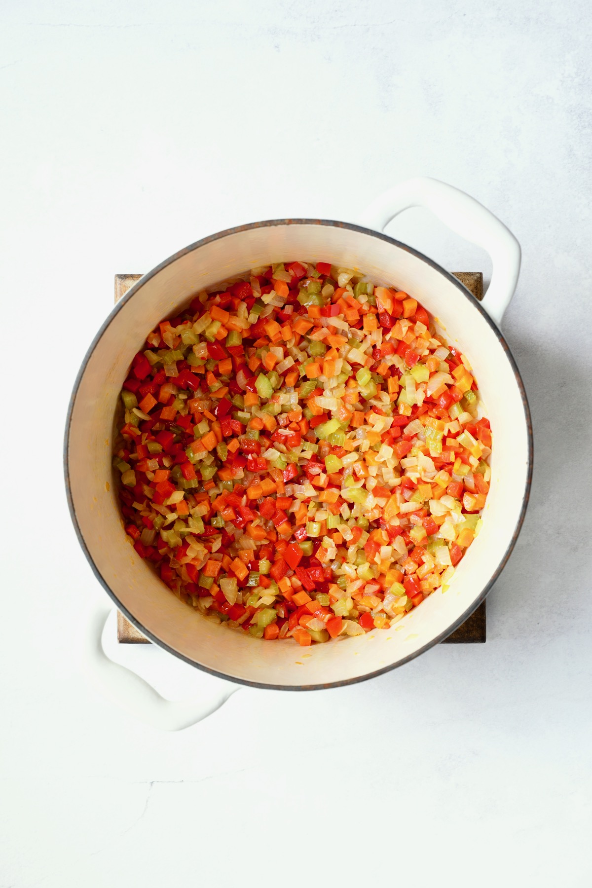 Cooked vegetables for soup in white Dutch oven.