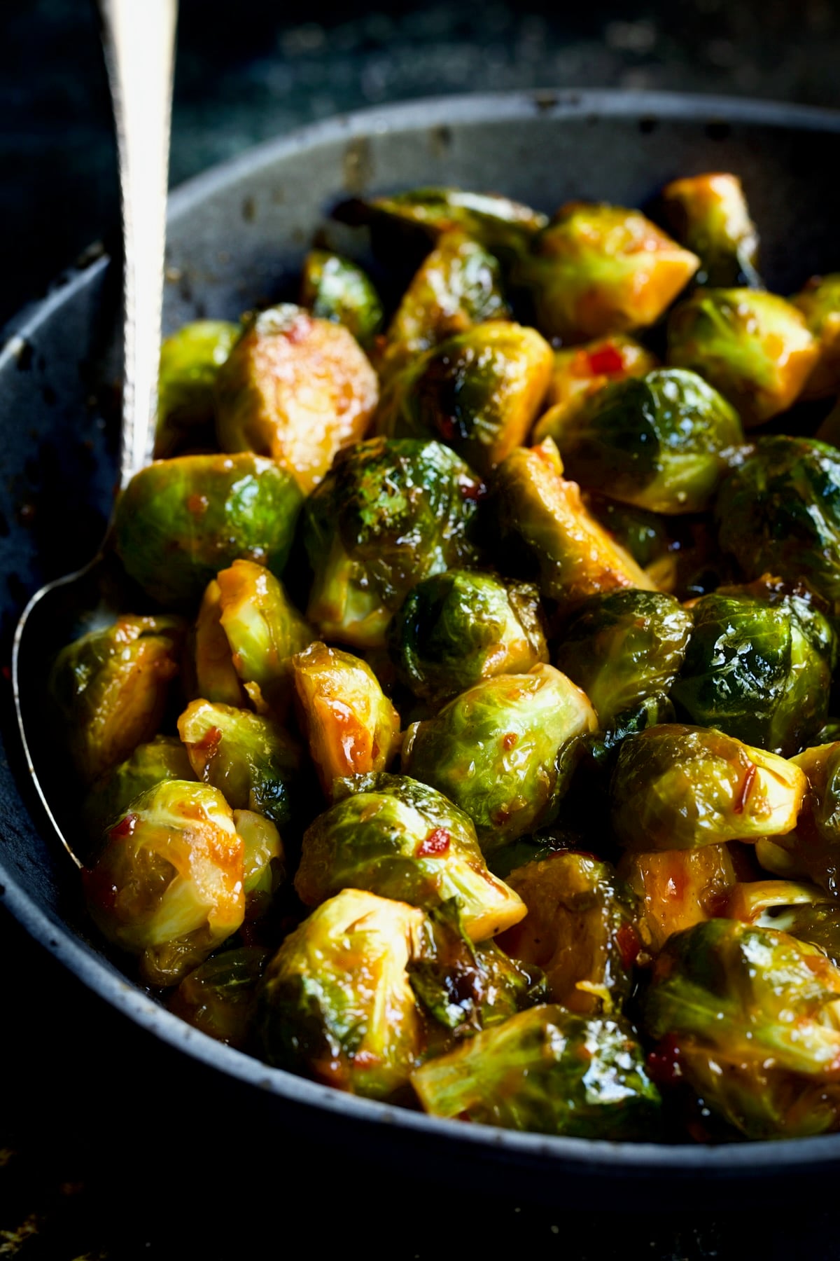 Sriracha Sweet Chili Roasted Brussels Sprouts in gray speckled bowl with serving spoon.