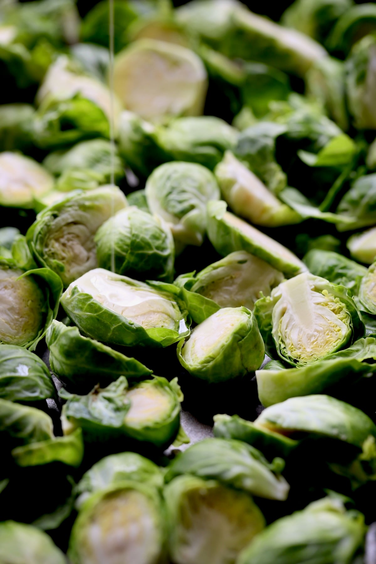 Halved Brussels sprouts on baking sheet being drizzled with oil.