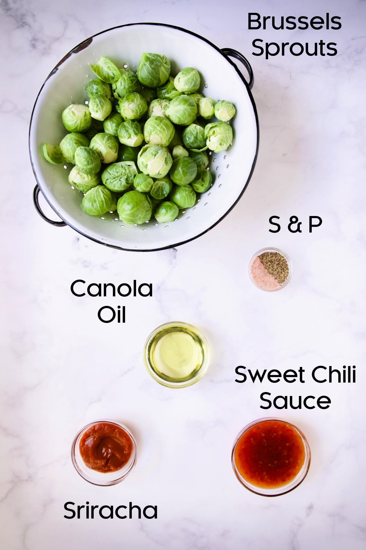 Ingredients for Sriracha Sweet Chili Roasted Brussels Sprouts with Brussels sprouts in white distressed colander and remaining ingredients in glass bowls.