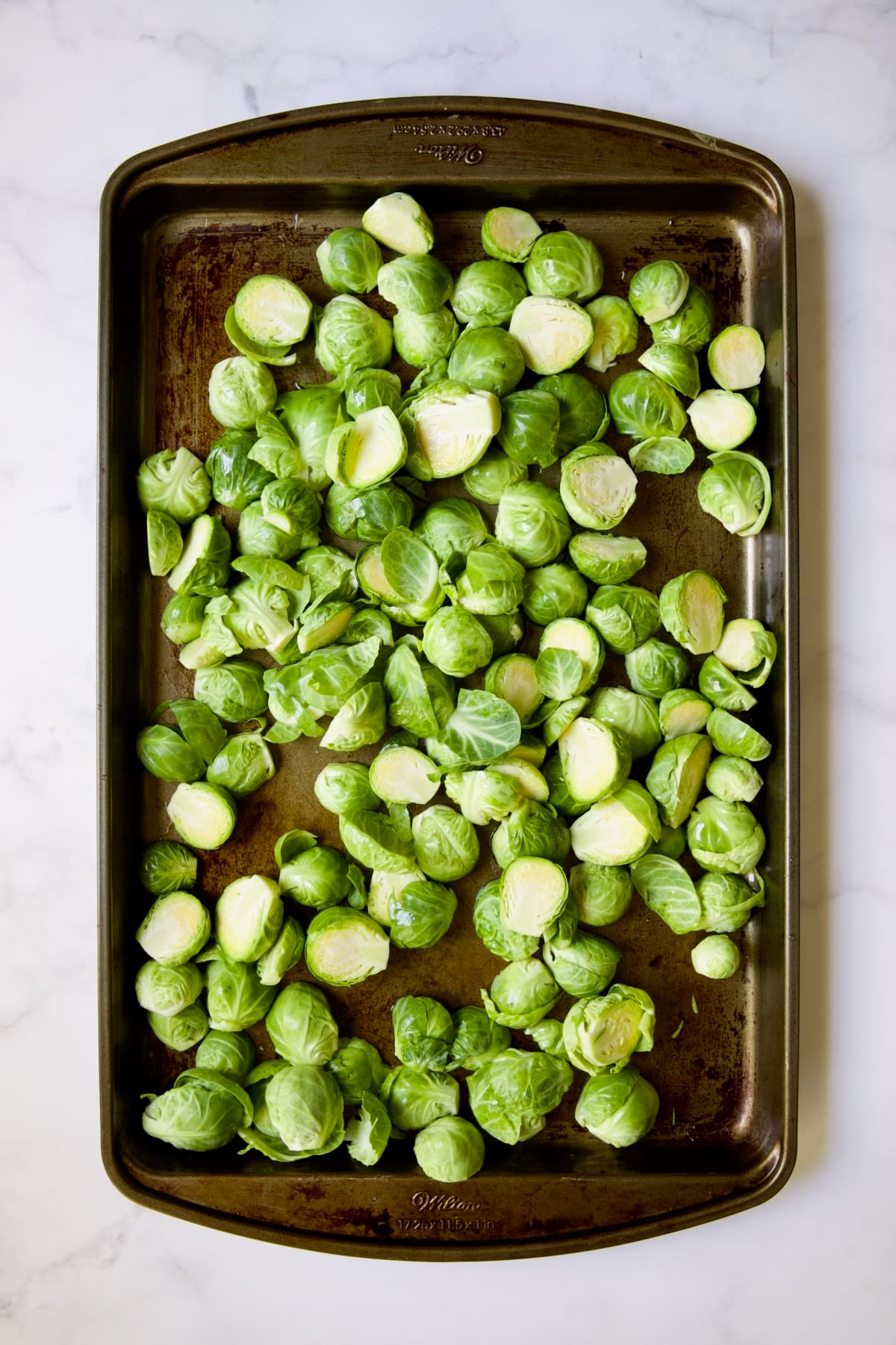 Halved Brussels sprouts on baking sheet before being roasted.