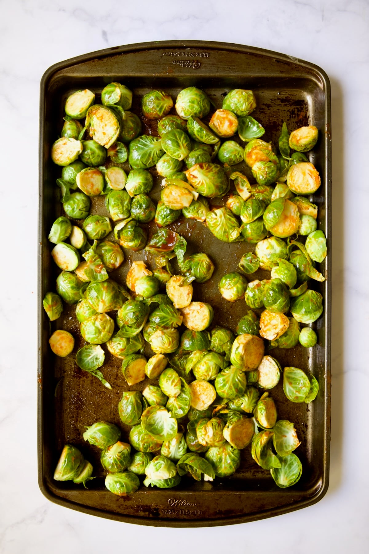 Halved Brussels sprouts on baking sheet before being roasted with Sriracha poured over them.