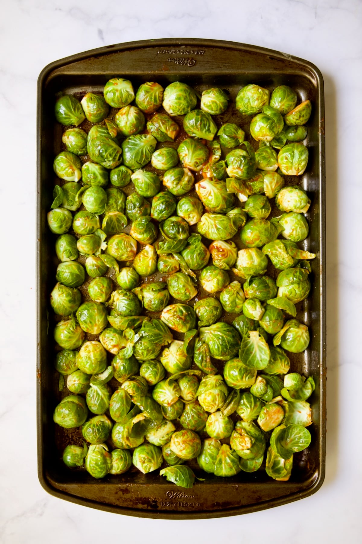 Halved Brussels sprouts on baking sheet before being roasted with Sriracha poured over them all facing cut side down.