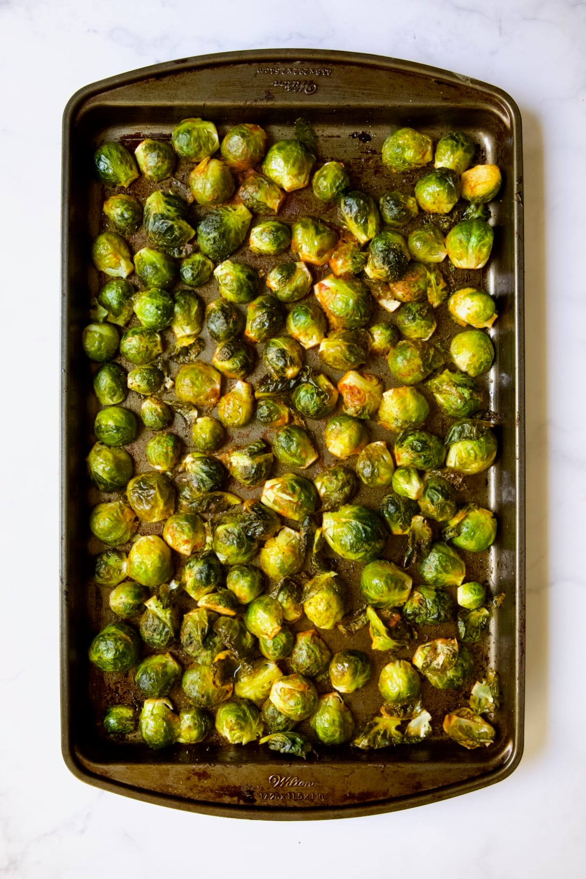 Halved Brussels sprouts on baking sheet after being roasted still facing cut side down.