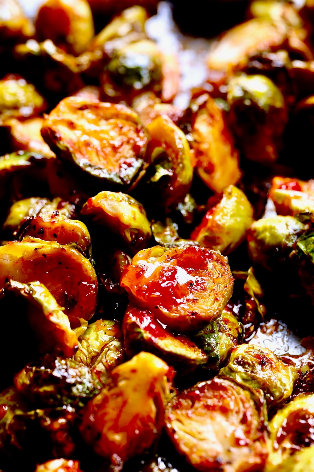 Halved Brussels sprouts on baking sheet drizzled with sweet chili sauce.