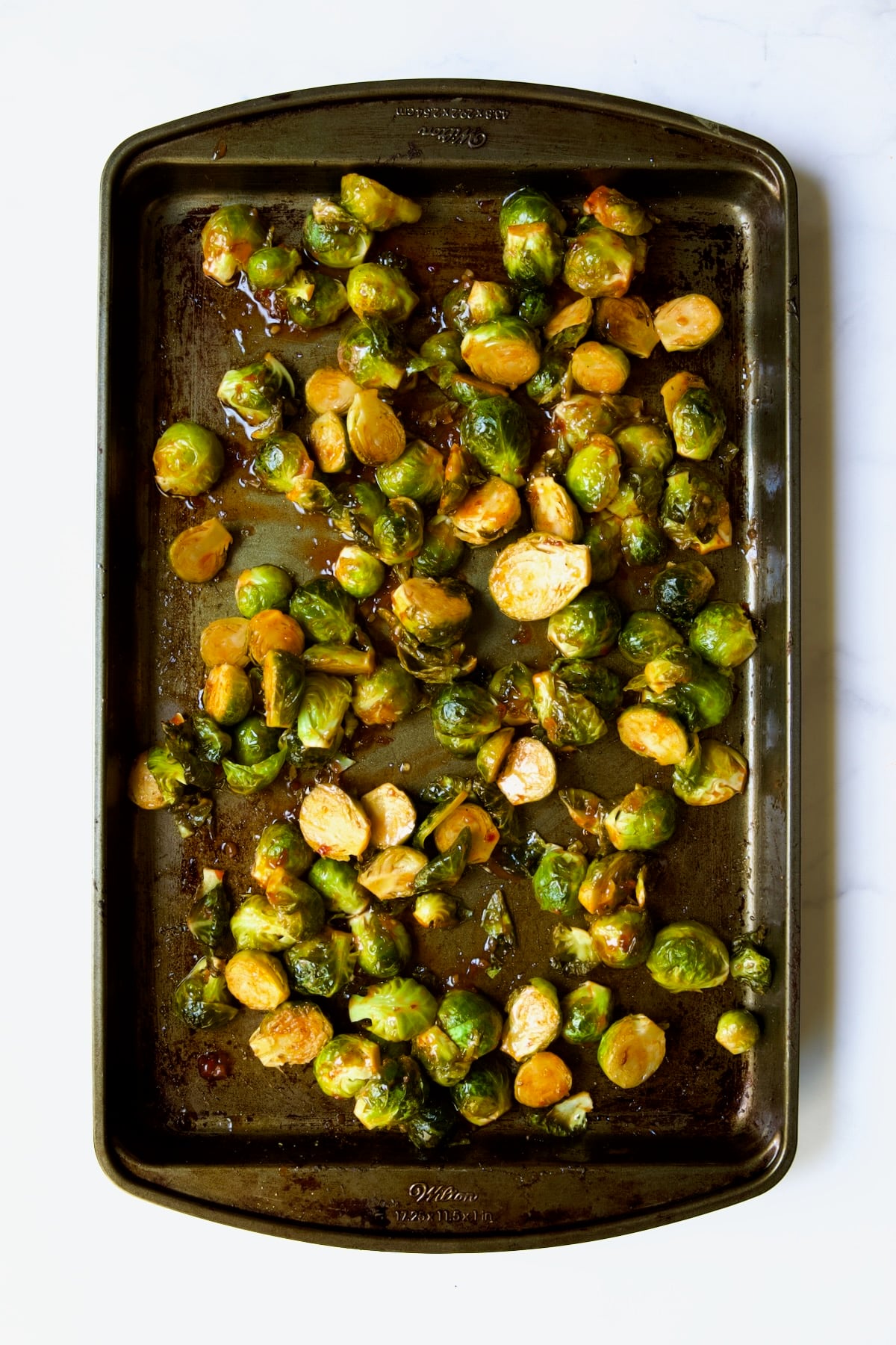 Halved Brussels sprouts on baking sheet drizzled with sweet chili sauce and stirred.