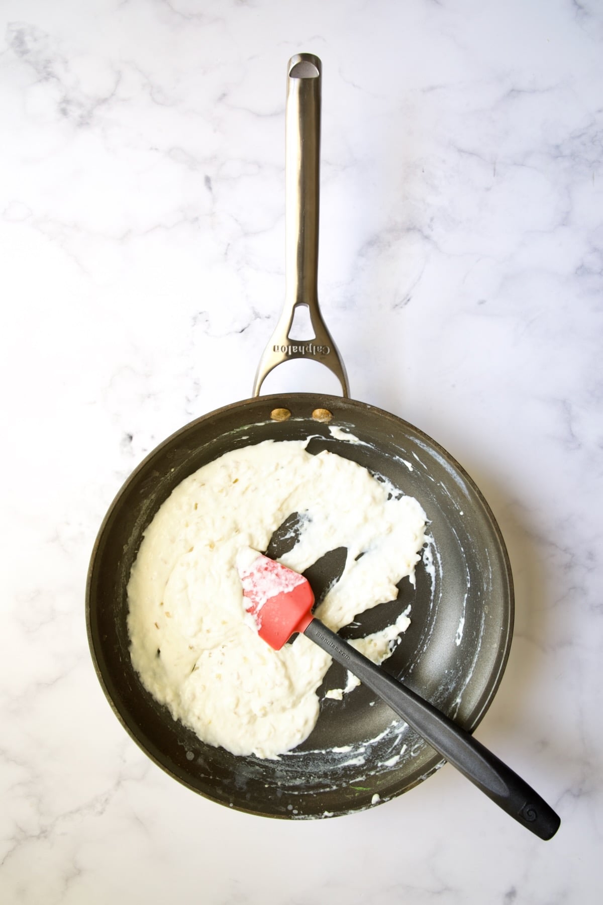 Thickened half and half in nonstick skillet being stirred with red and black rubber spatula.