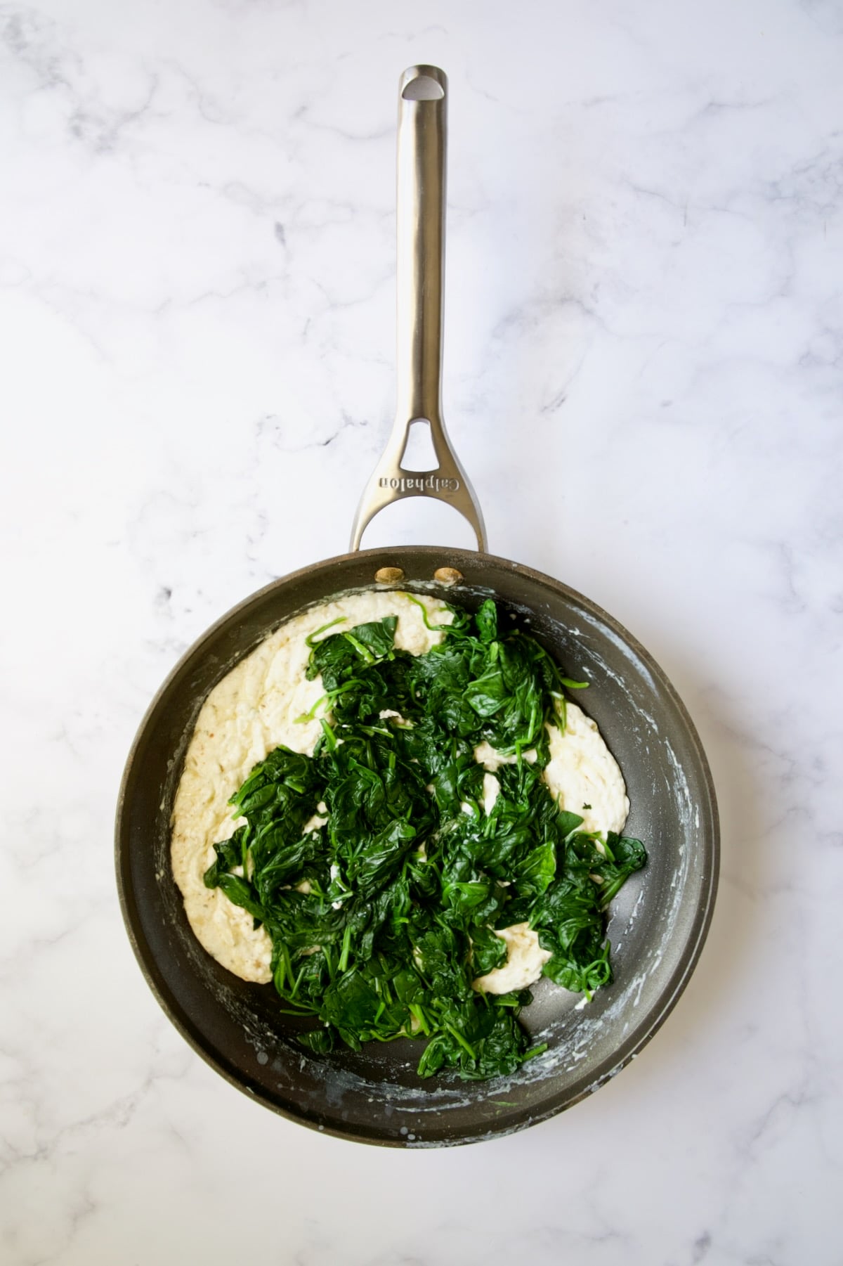 Wilted spinach added to cheese sauce in nonstick skillet.