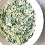 Steakhouse Creamed Spinach in white oval bowl with serving spoon.
