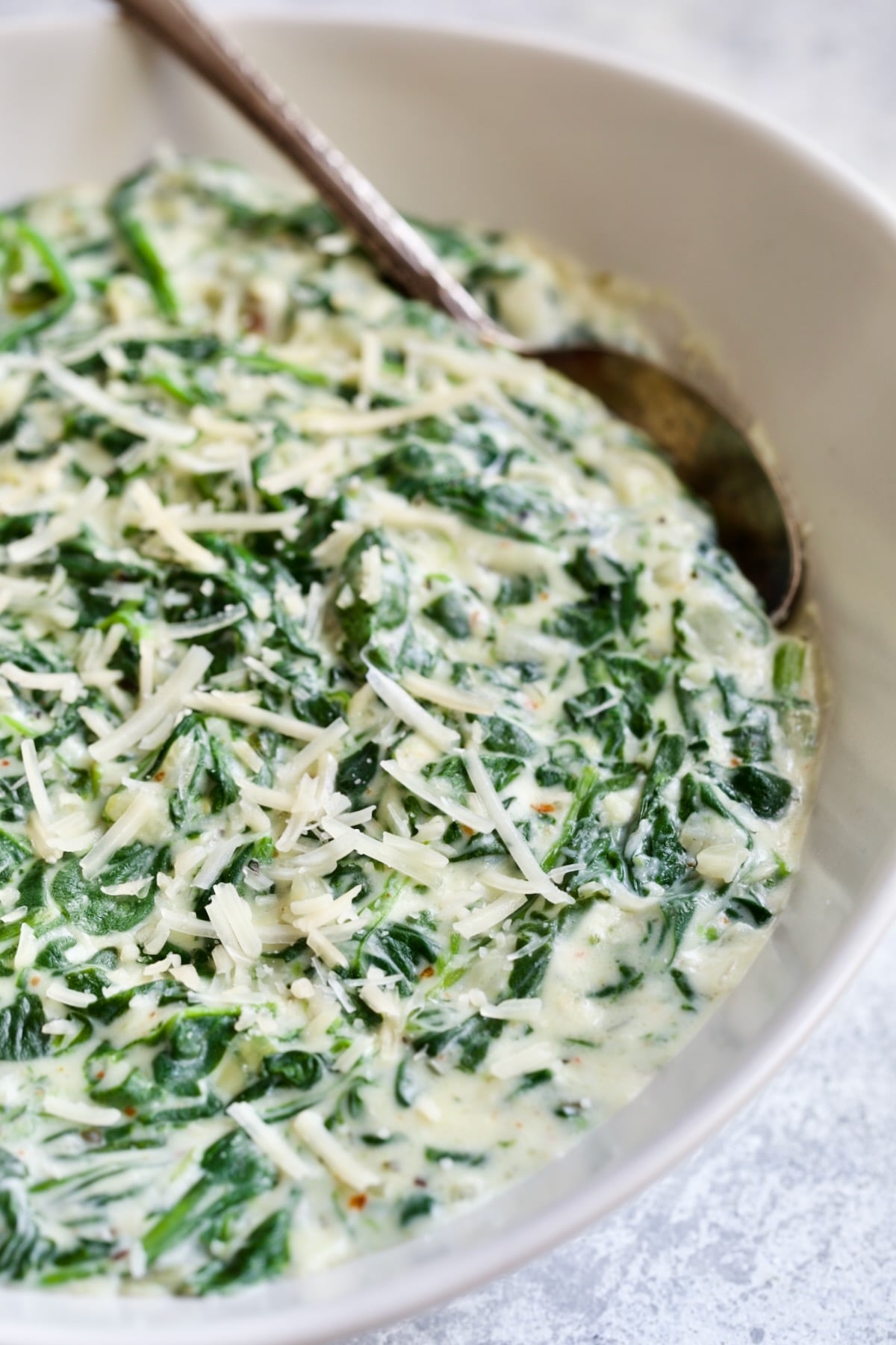 Steakhouse Creamed Spinach in white oval bowl with serving spoon.