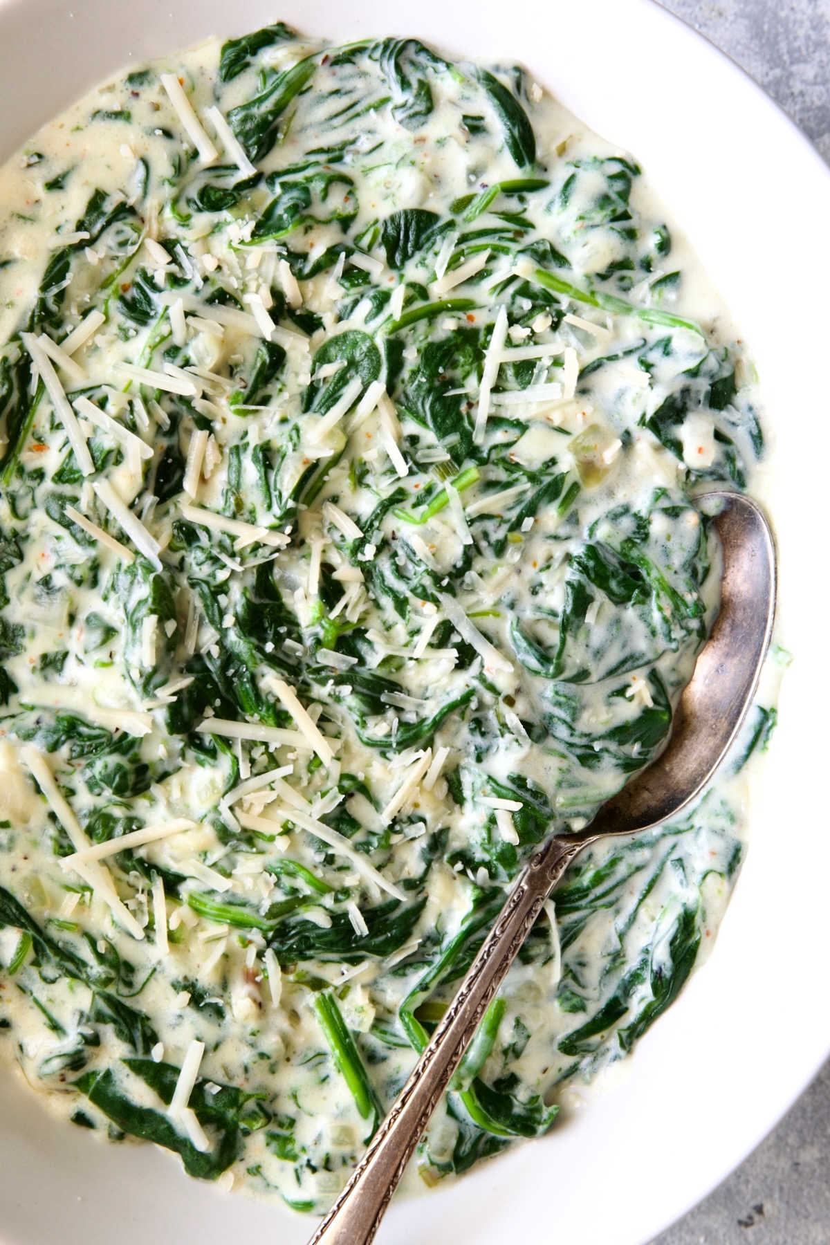 Steakhouse Creamed Spinach in white oval bowl with serving spoon.