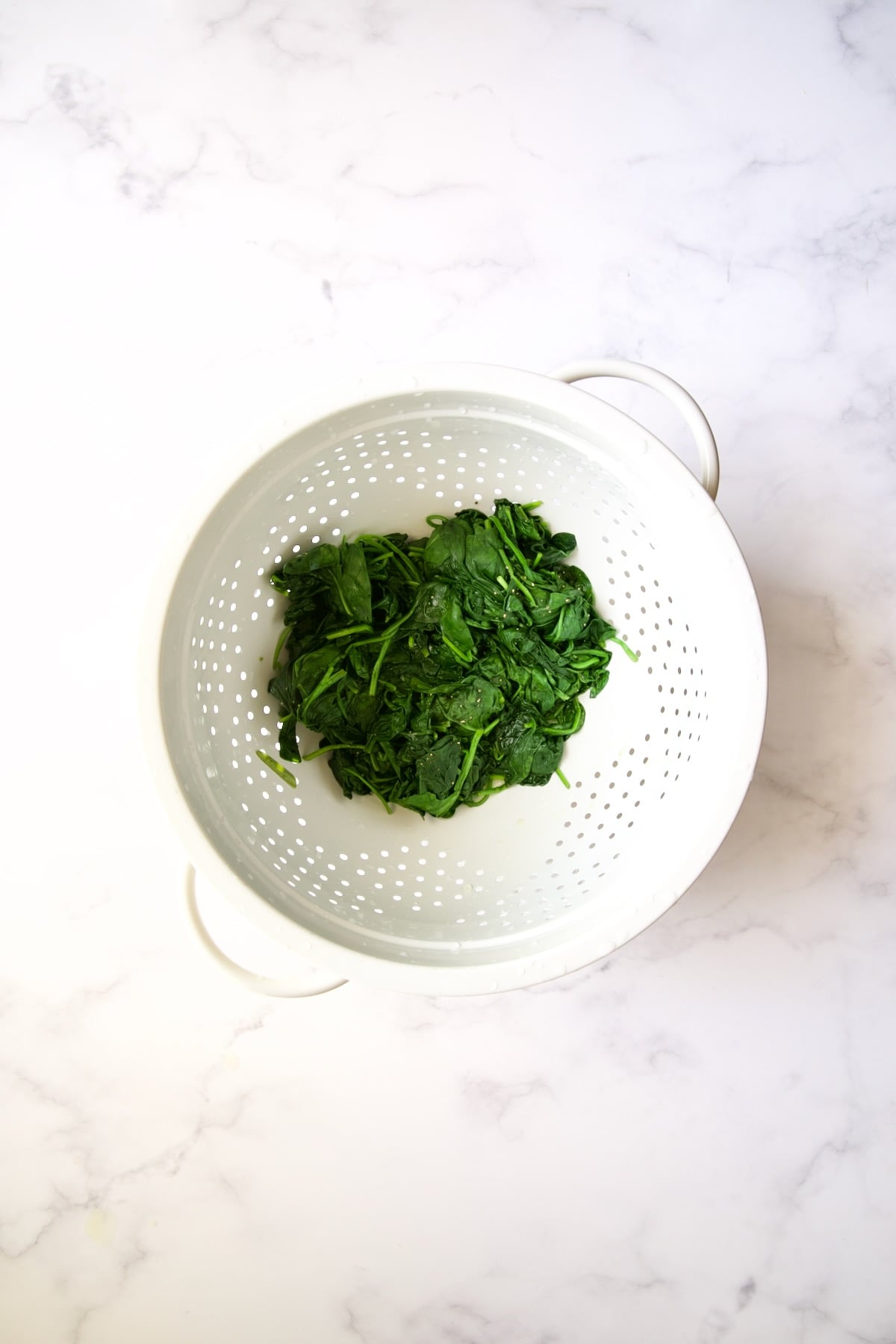 Wilted baby spinach in white colander.