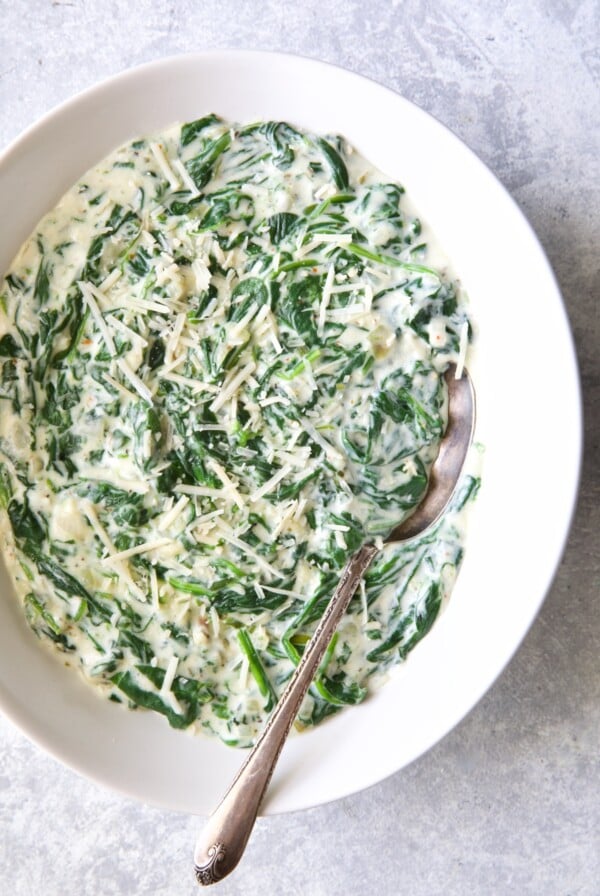 Steakhouse Creamed Spinach in white oval bowl with serving spoon.