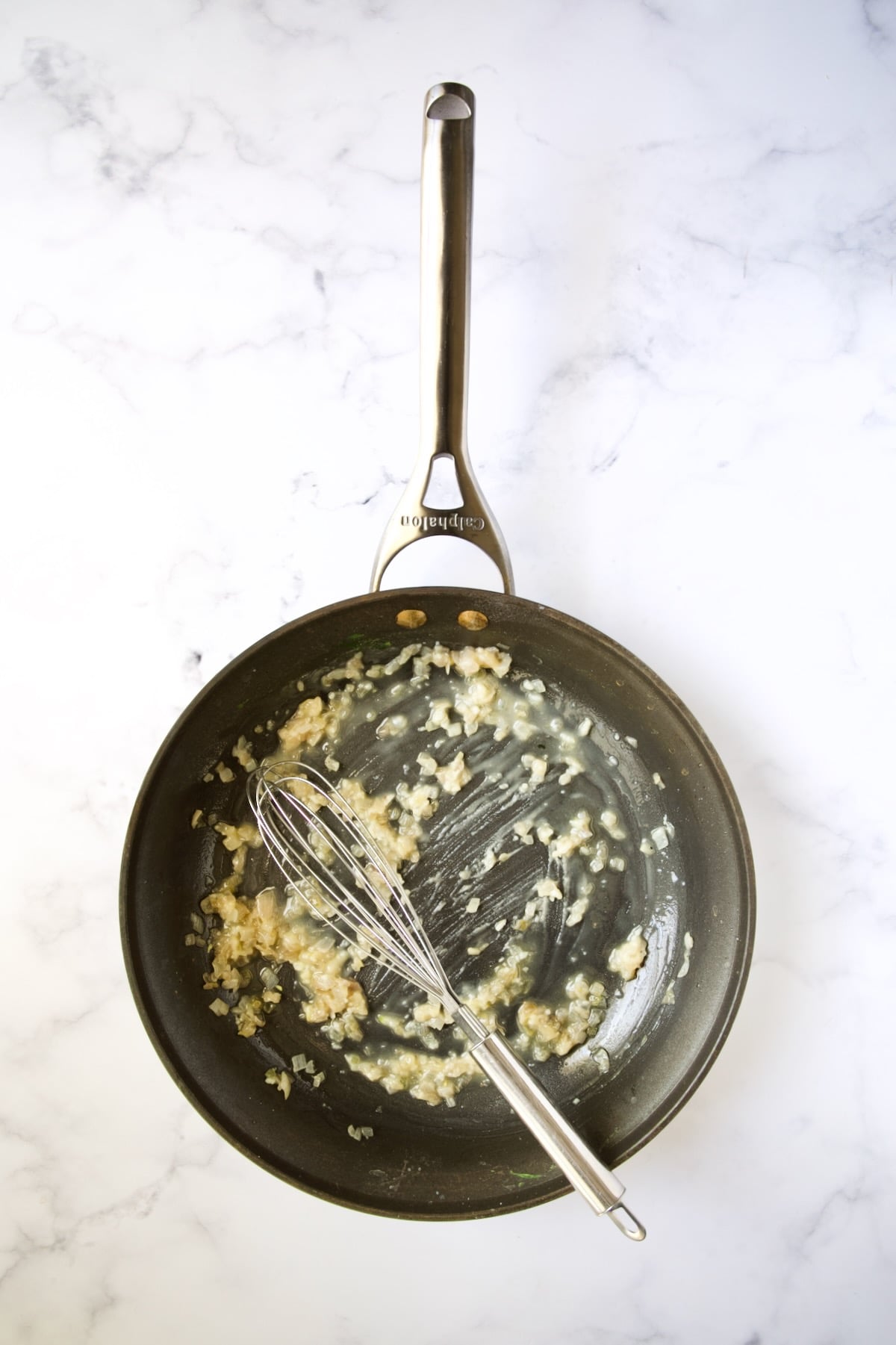 Cooked shallots and flour being whisked with wire whisk in nonstick skillet.