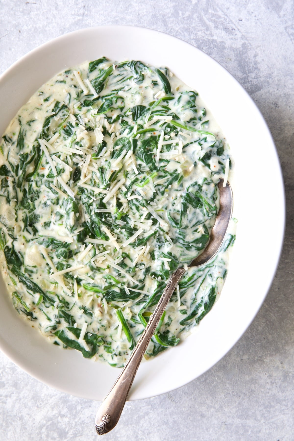 Steakhouse Creamed Spinach in white oval bowl with serving spoon.