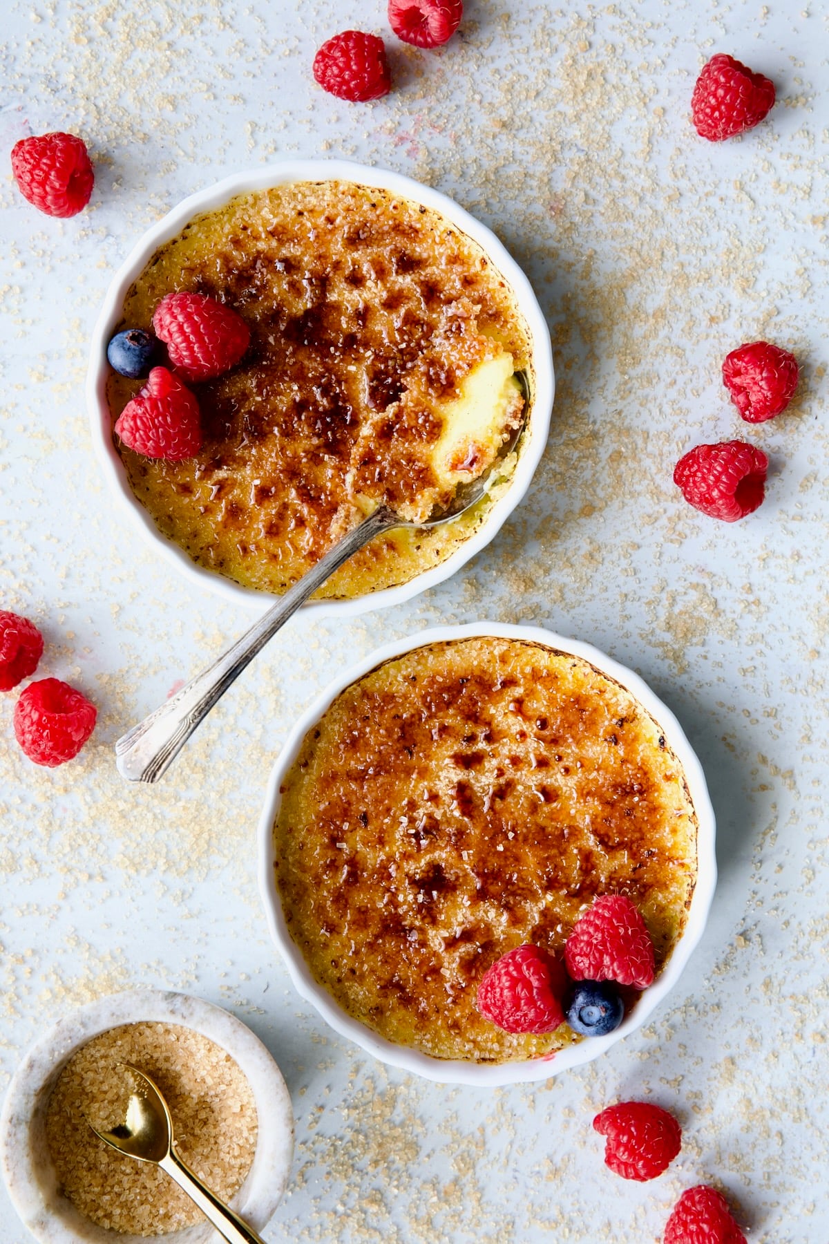 Two dishes of Classic Creme Brulee for Two garnished with red raspberries adn blueberries.