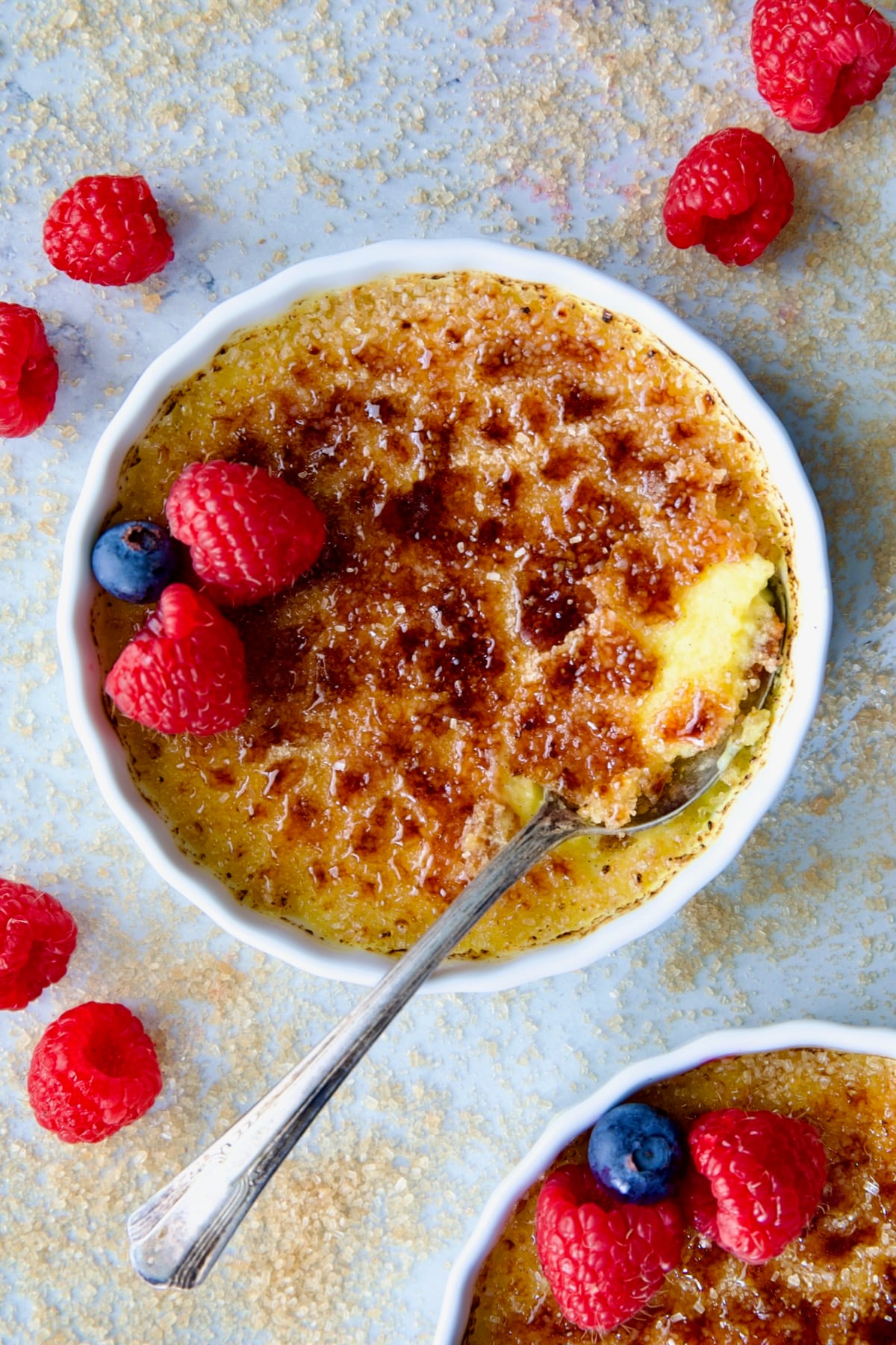 One dish of Classic Creme Brulee for Two garnished with red raspberries and blueberries.
