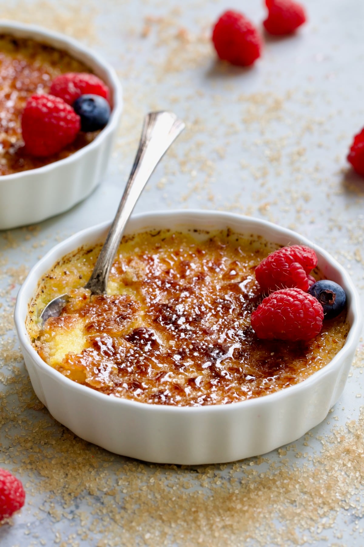 One dish of Classic Creme Brulee for Two on sugary surface garnished with red raspberries and blueberries.