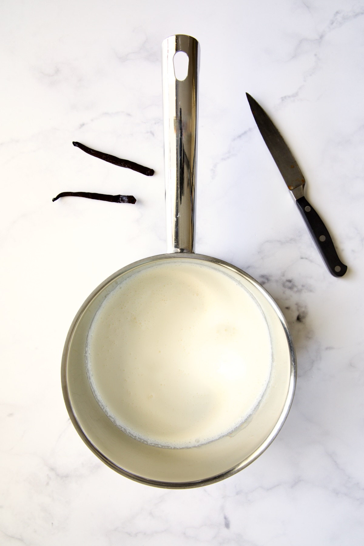 Heavy cream in stainless steel saucepan with vanilla bean cut in half and pairing knife.