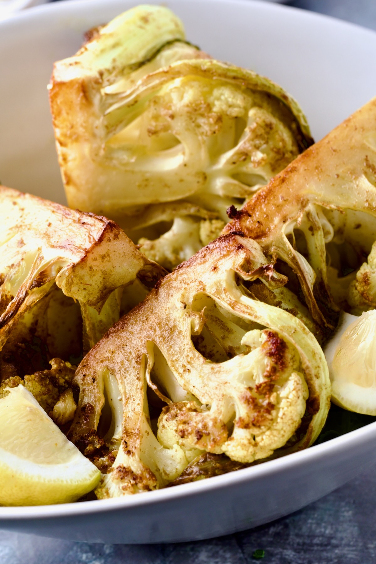 Curry Roasted Cauliflower Wedges in white bowl with lemon wedge.