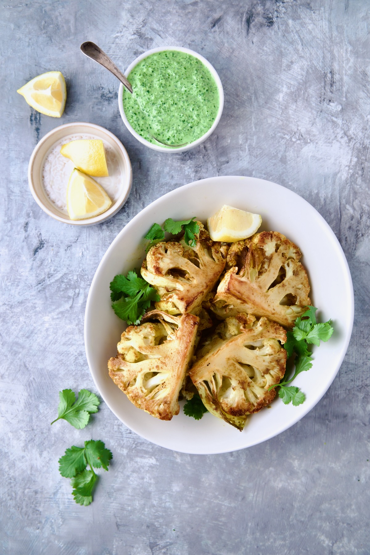 Curry Roasted Cauliflower Wedges with Cilantro Chutney and bowl of lemon wedges garnished with fresh cilantro.