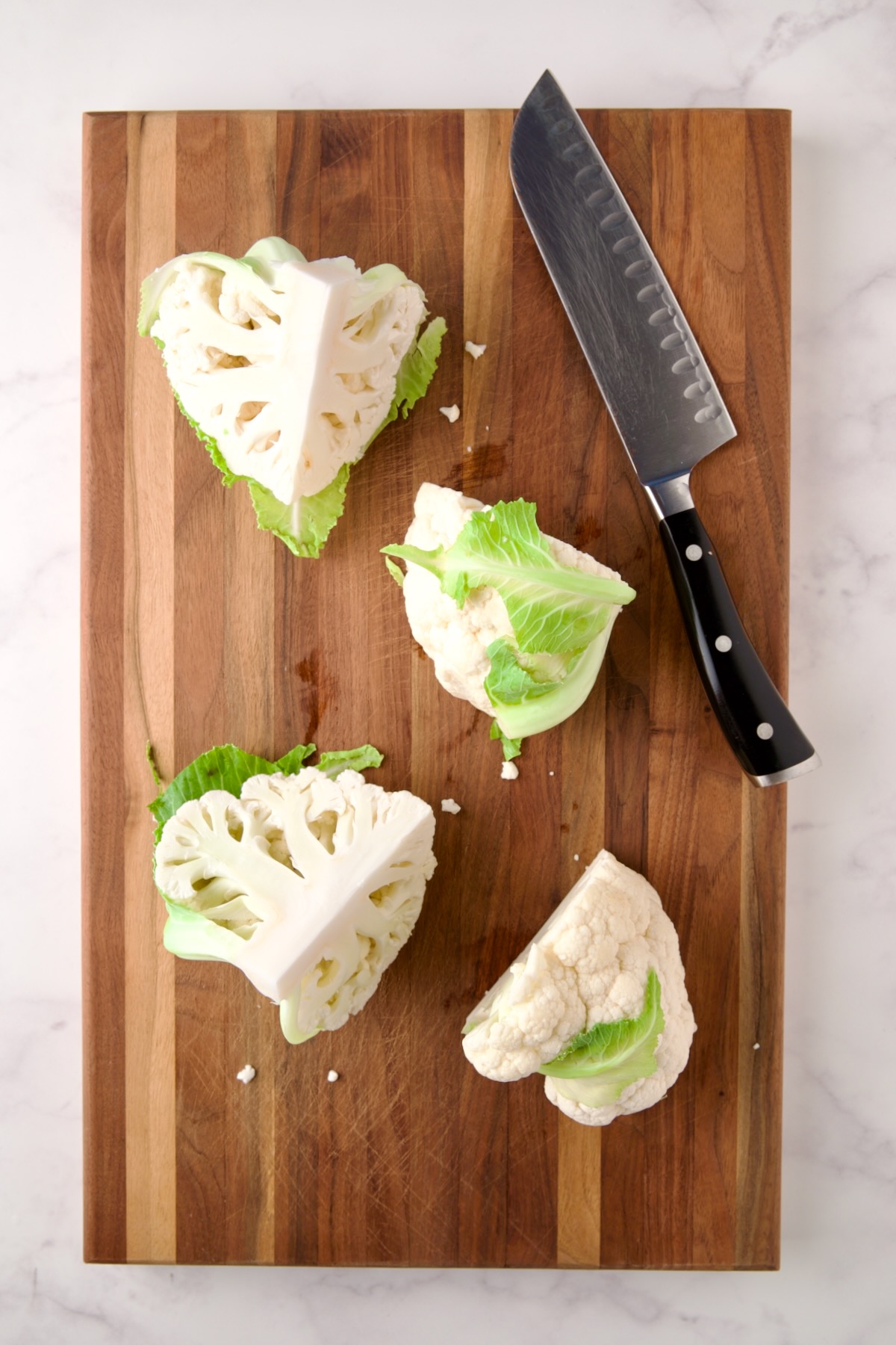 Four wedges of cauliflower on wood cutting board with chef's knife.