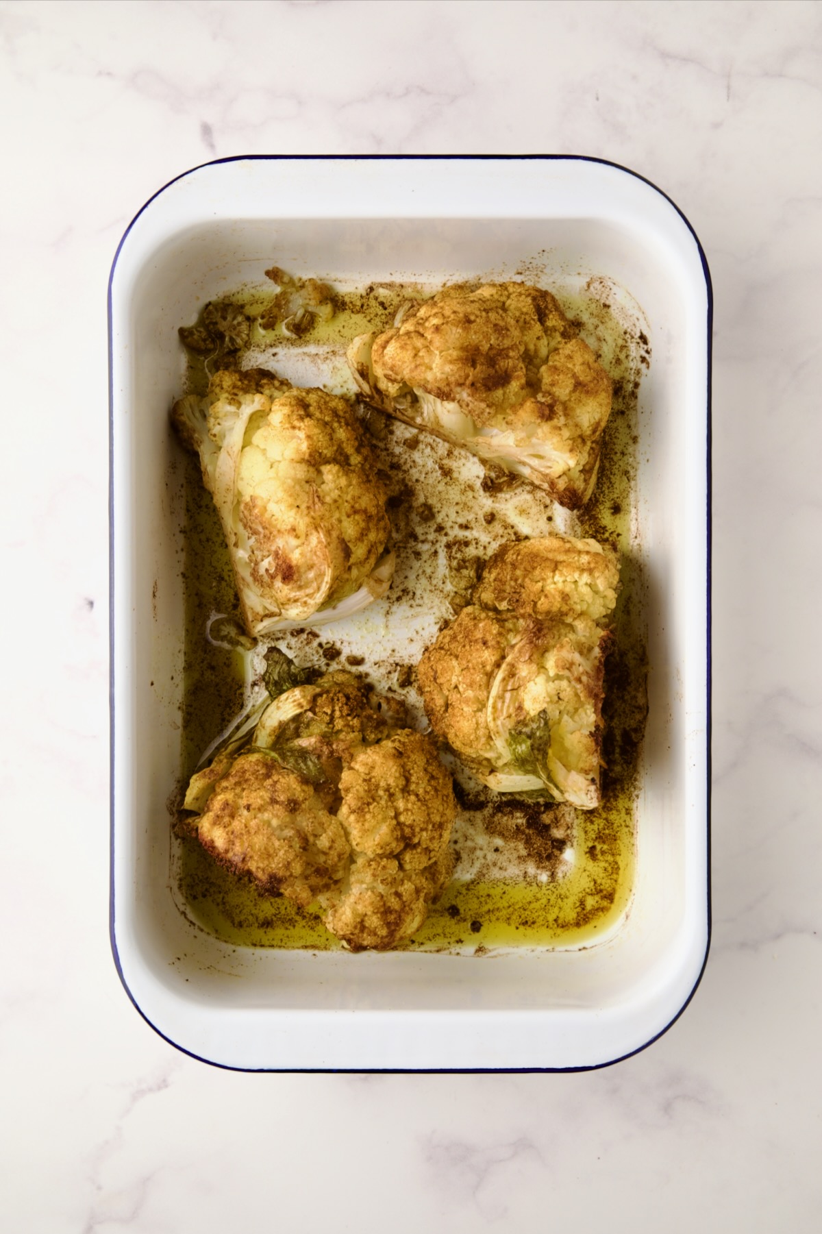 Four roasted wedges of cauliflower in white roasting pan.