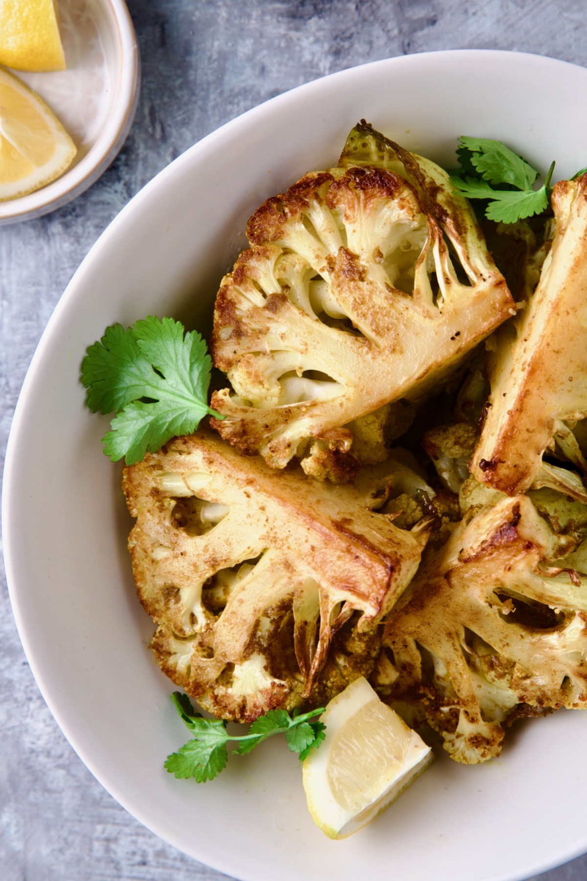 Wedges of Curry Roasted Cauliflower in white oval bowl with lemon wedges.