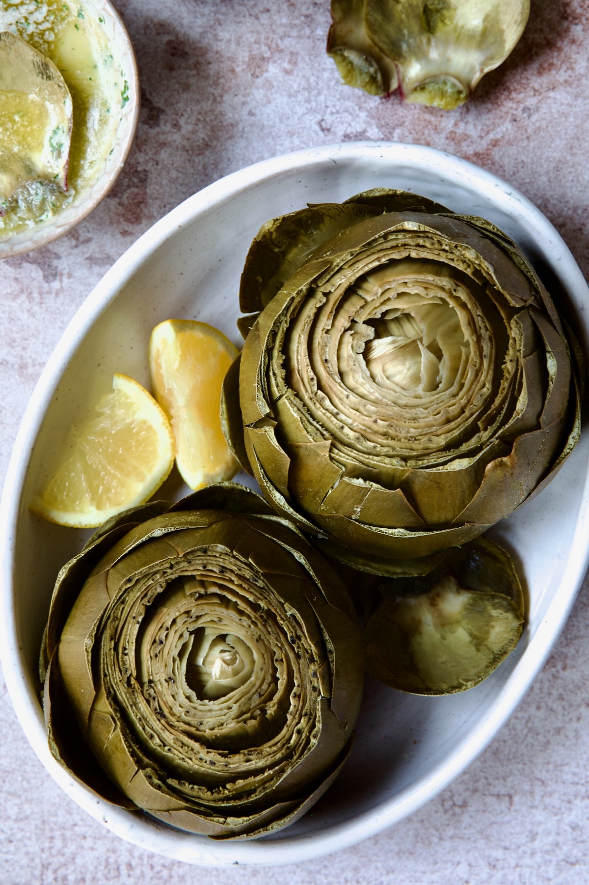 Instant Pot Artichokes (With Garlic Butter) in white oval bowl with lemon wedges.