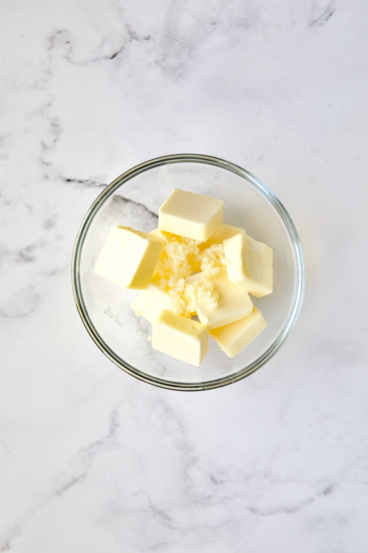 Butter slices and minced garlic in glass bowl.