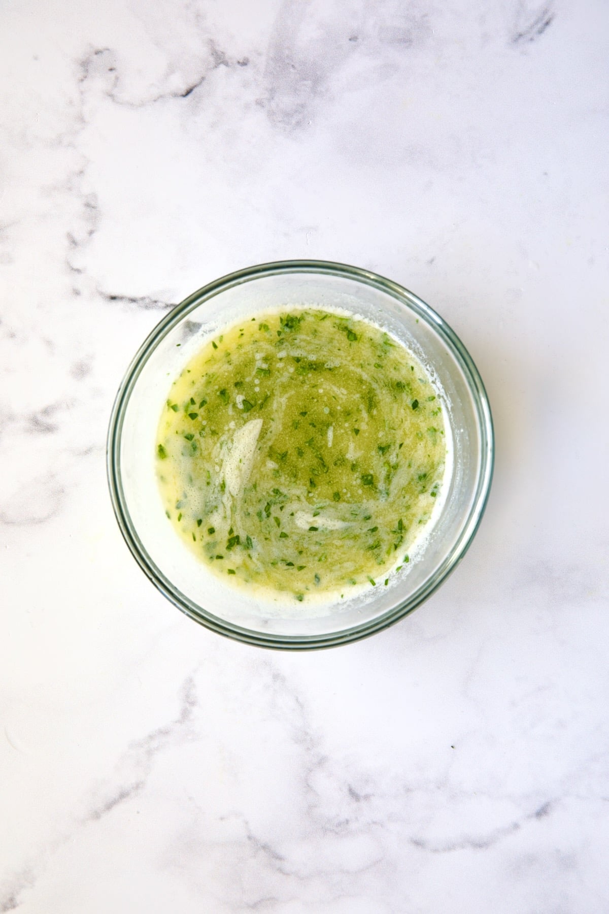 Melted butter with parsley added in glass bowl.
