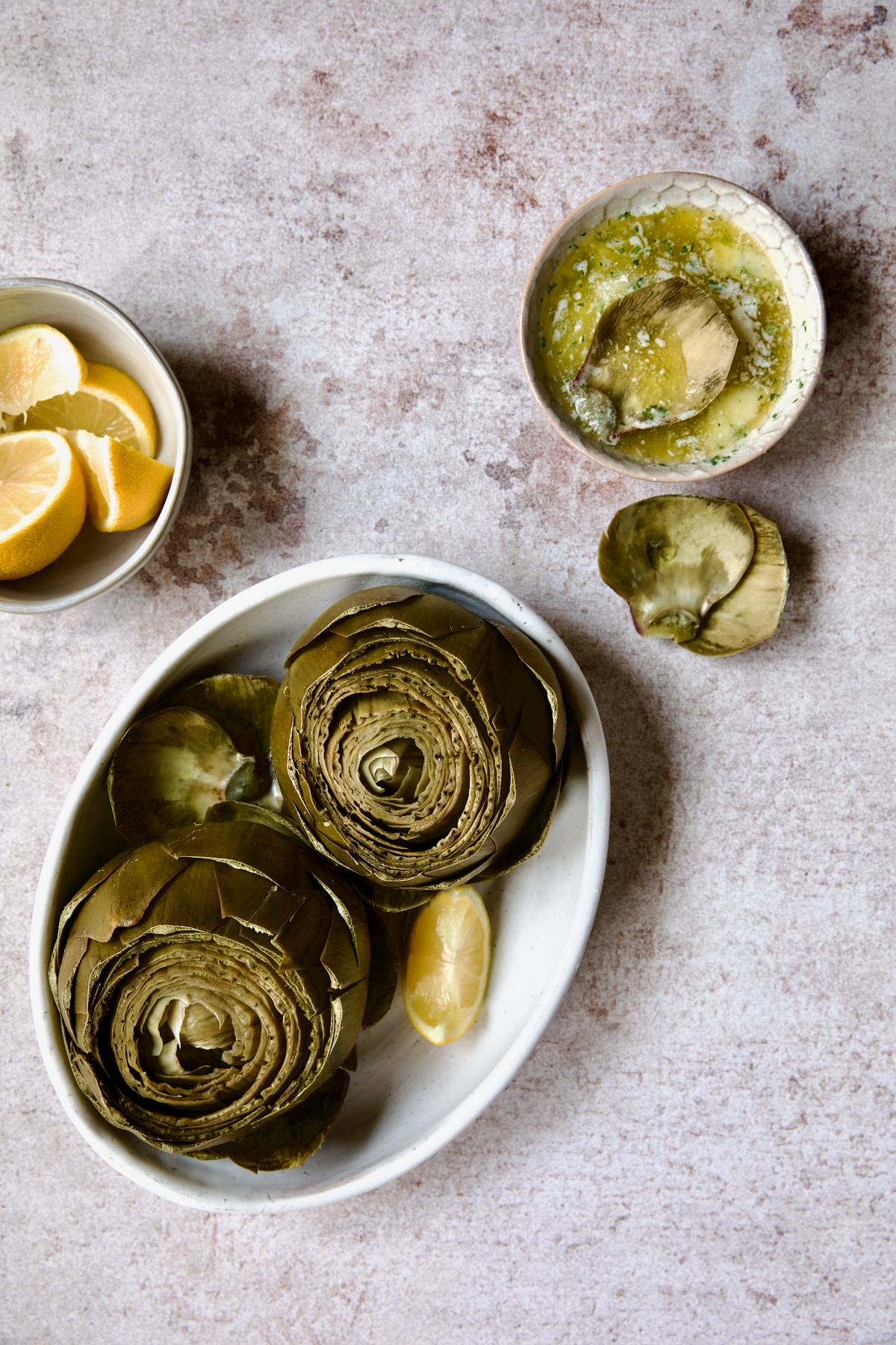 Instant Pot Artichokes in white oval serving bowl with Garlic Butter and lemon wedges.