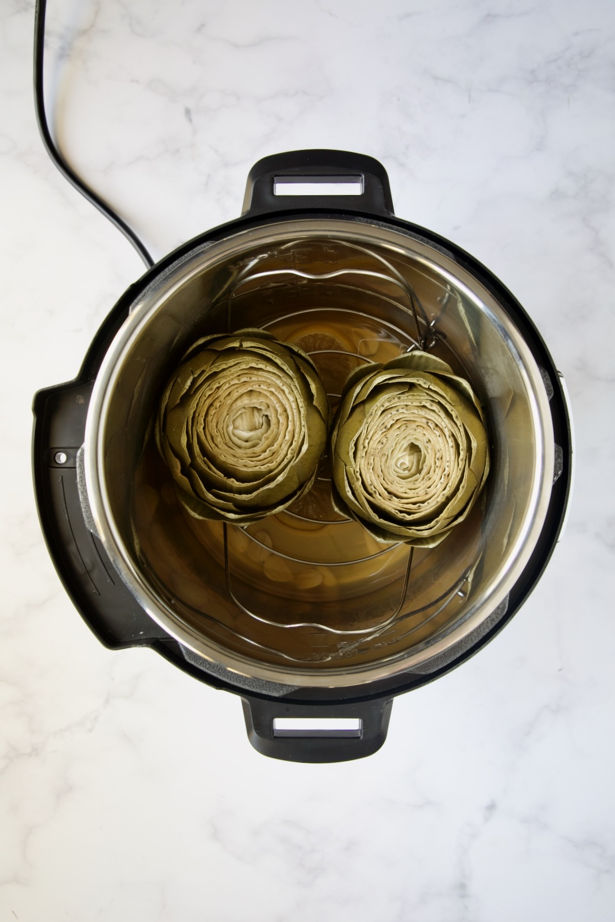 Two cooked artichokes in Instant Pot.