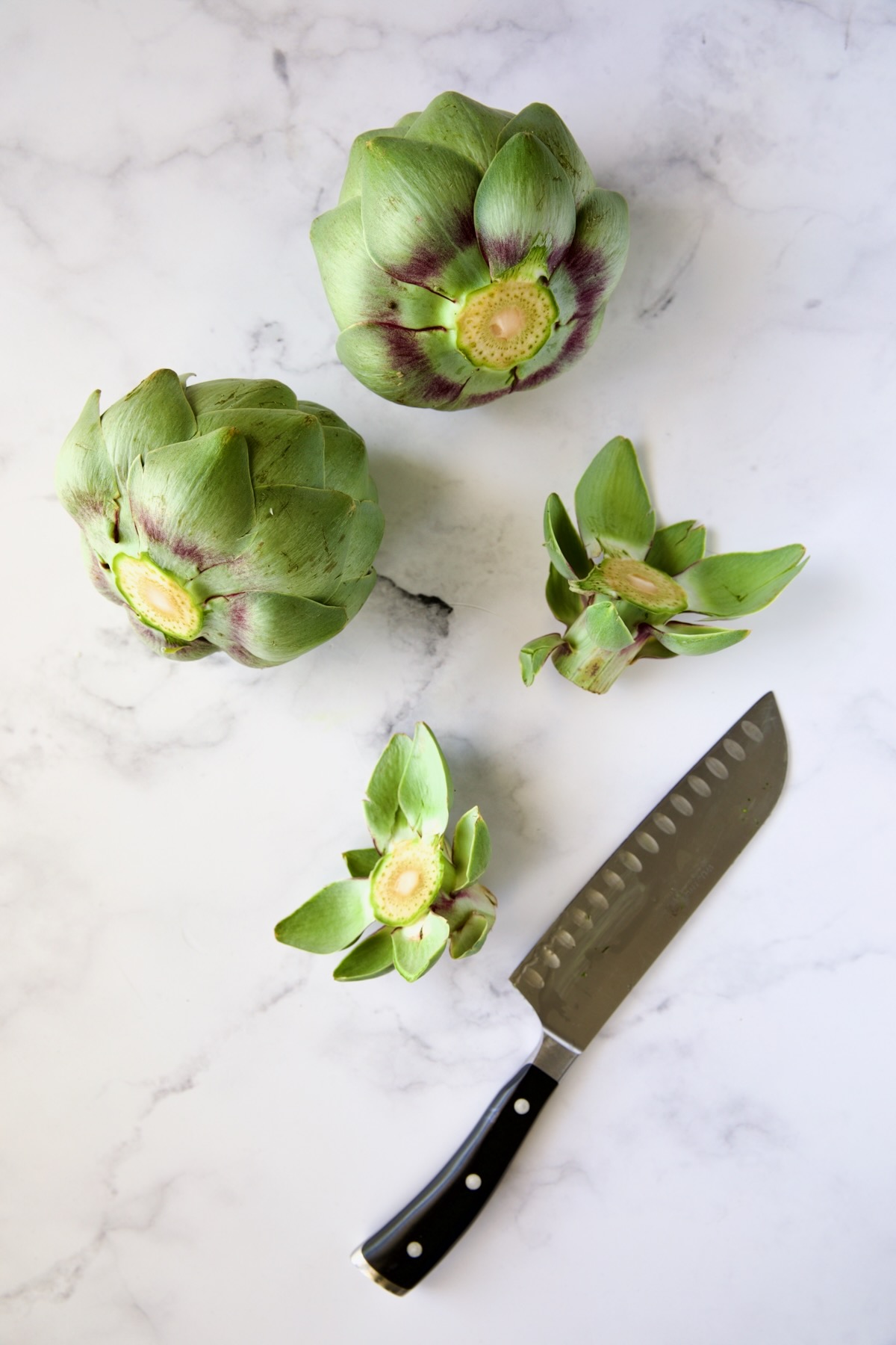 Two artichokes with stems removed by chef's knife.