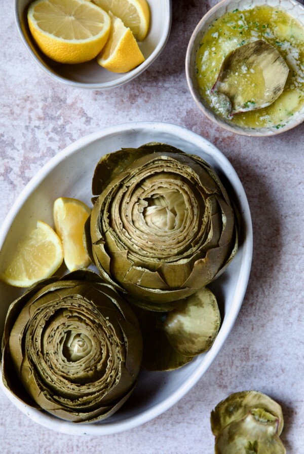 Instant Pot Artichokes (With Garlic Butter) in white oval serving bowl with lemon wedges.