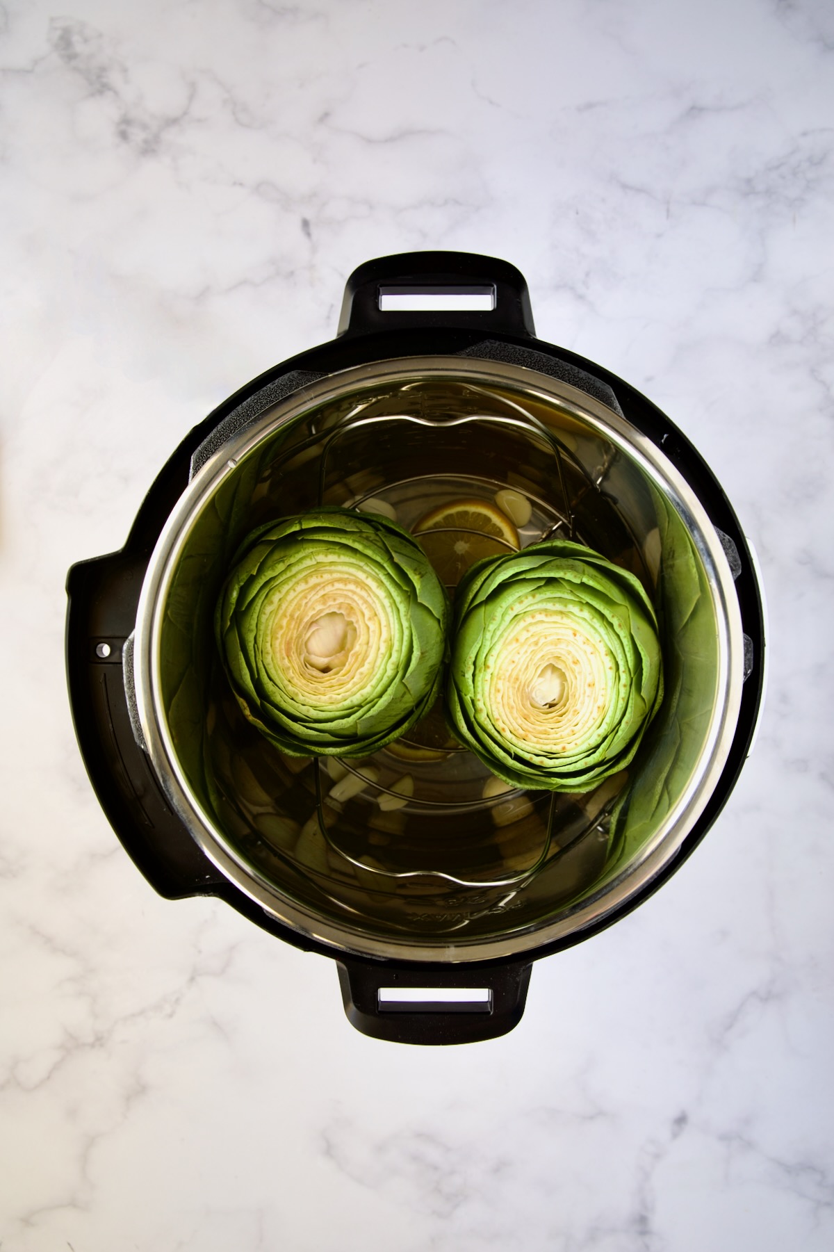 Uncooked artichokes set into Instant Pot.