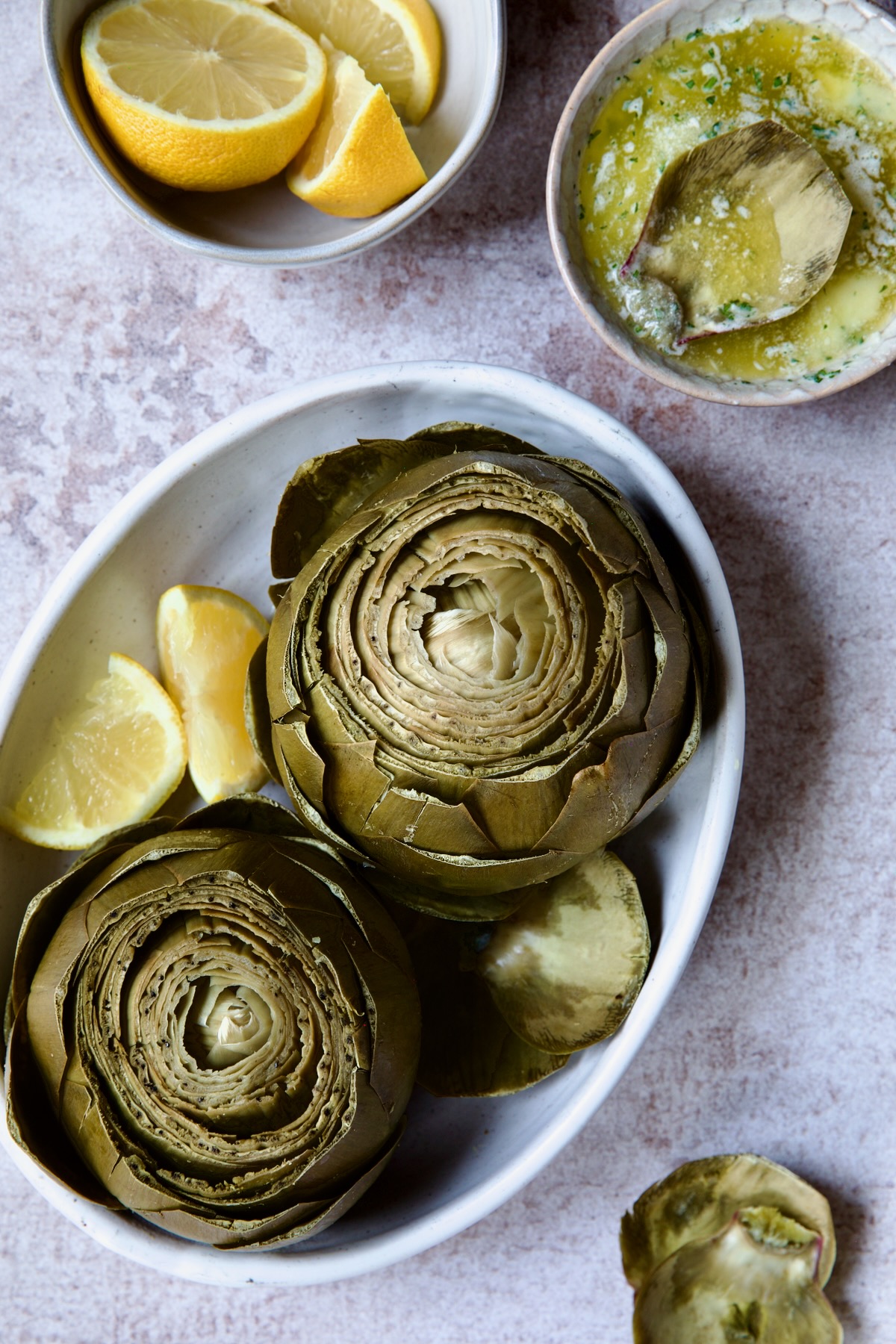 Instant Pot Artichokes (With Garlic Butter) in white oval serving bowl with lemon wedges.