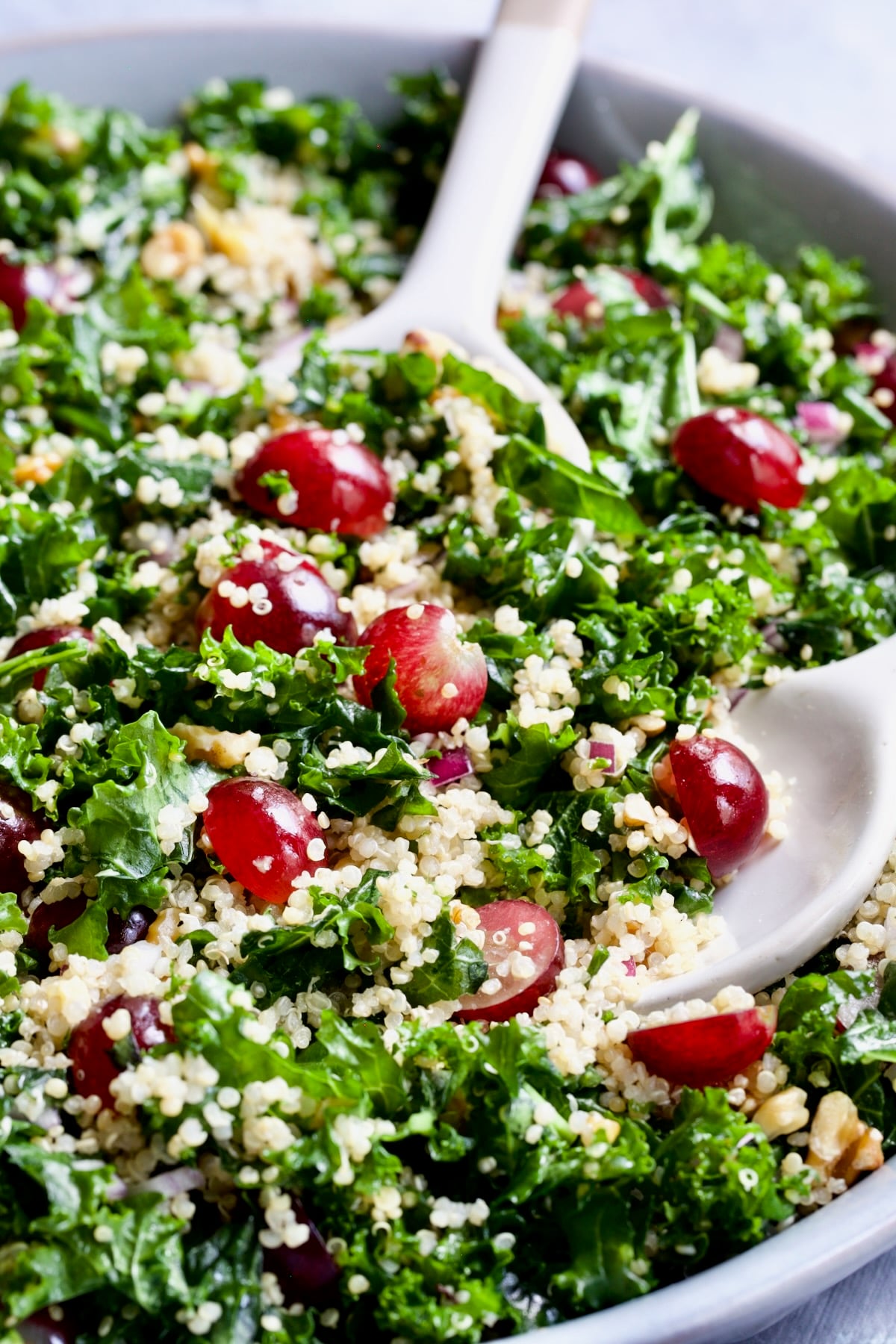 Kale Quinoa Salad with Lemon Honey Dressing being scooped up with serving utensils.
