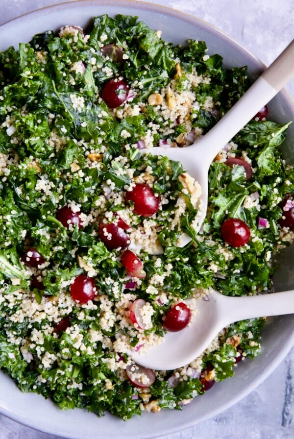 Kale Quinoa Salad with Lemon Honey Dressing in gray serving bowl with serving utensils.