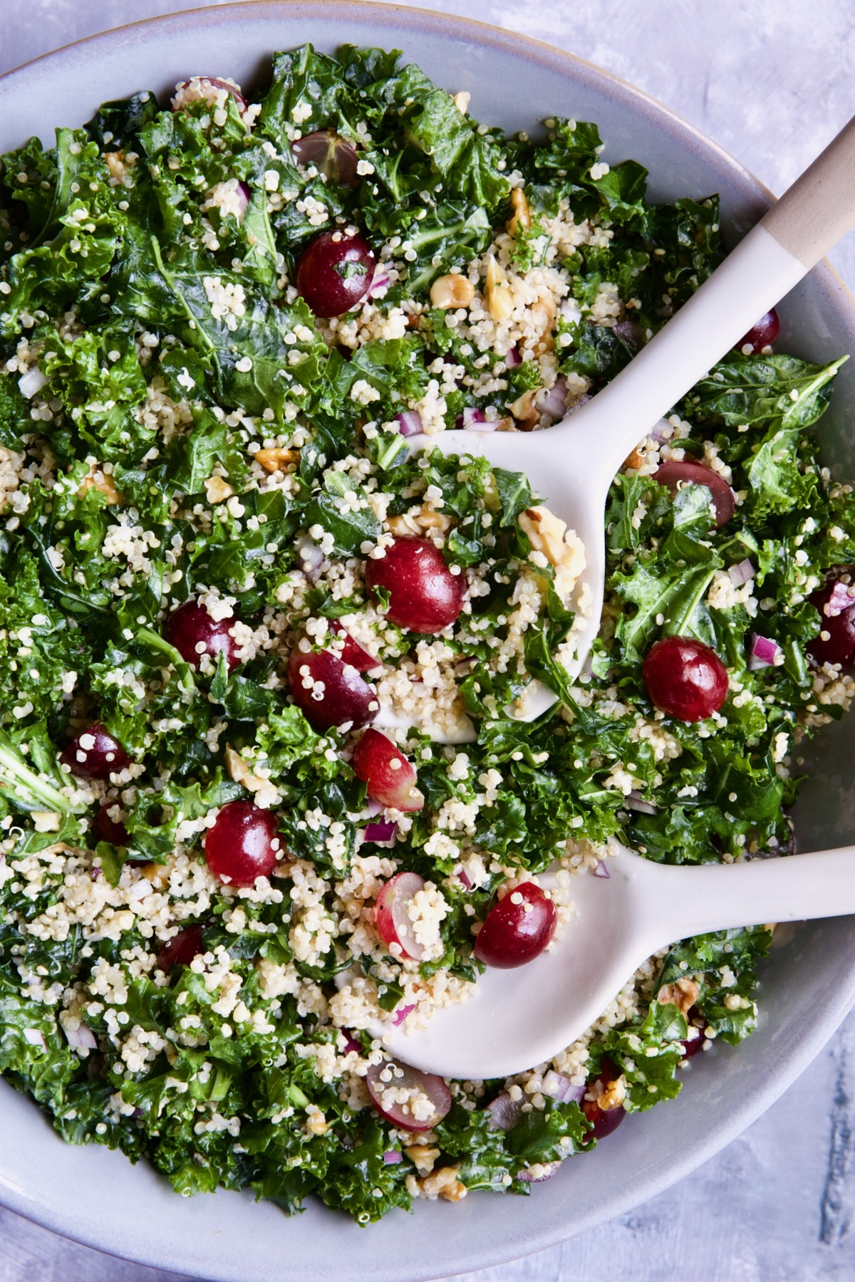 Kale Quinoa Salad with Lemon Honey Dressing in gray serving bowl with serving utensils.