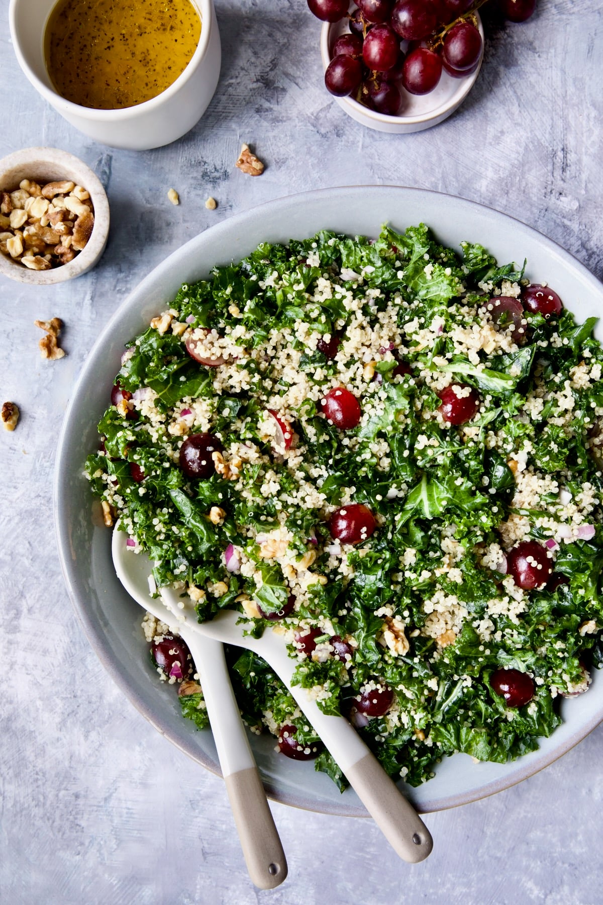 Kale Quinoa Salad with Lemon Honey Dressing in gray serving bowl with serving utensils.