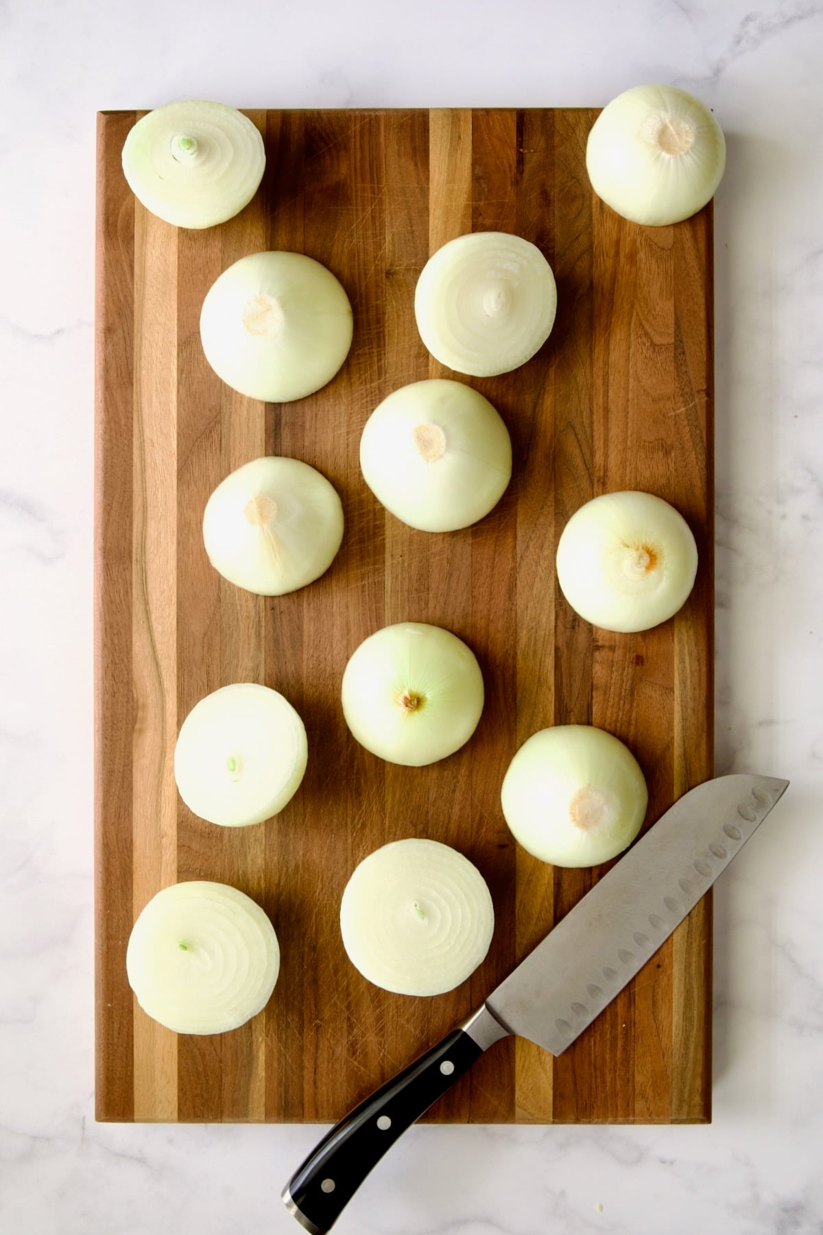 Peeled onions cut in half with chef knife on wood cutting board.