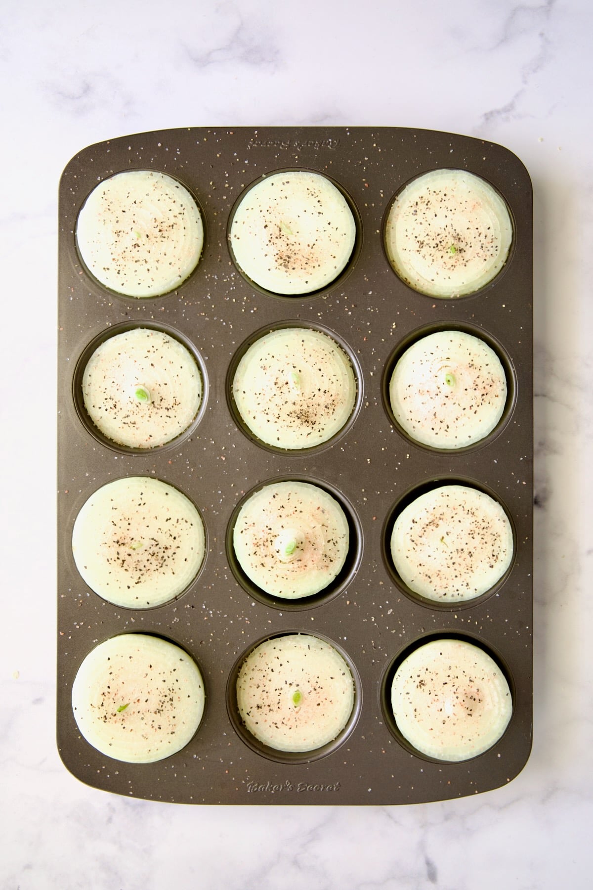 Onions halves in nonstick muffin pan sprinkled with black pepper.