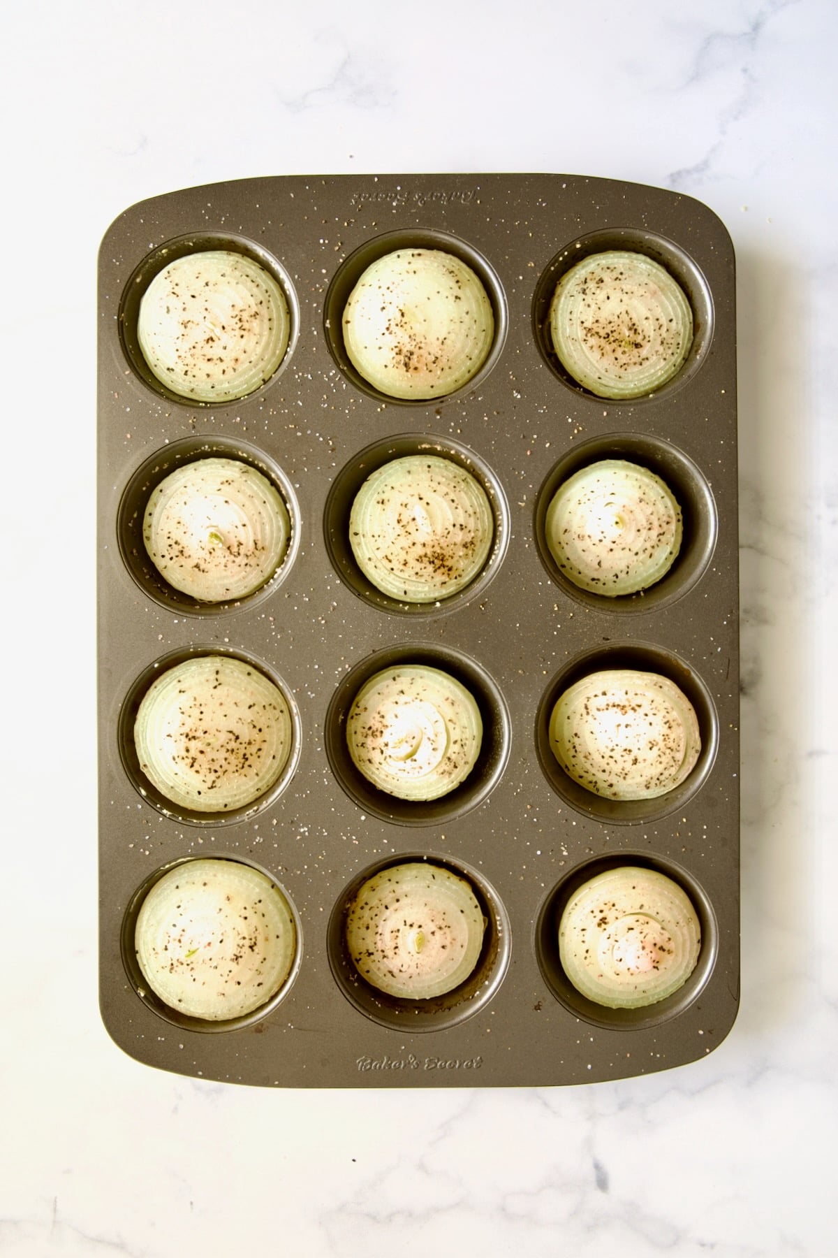 Onions halves in nonstick muffin pan after being baked for 20 minutes.