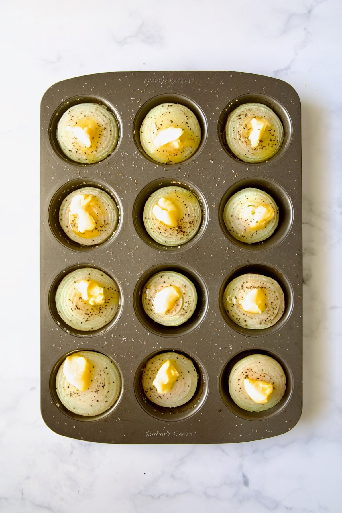 Onions halves in nonstick muffin pan topped with ghee.