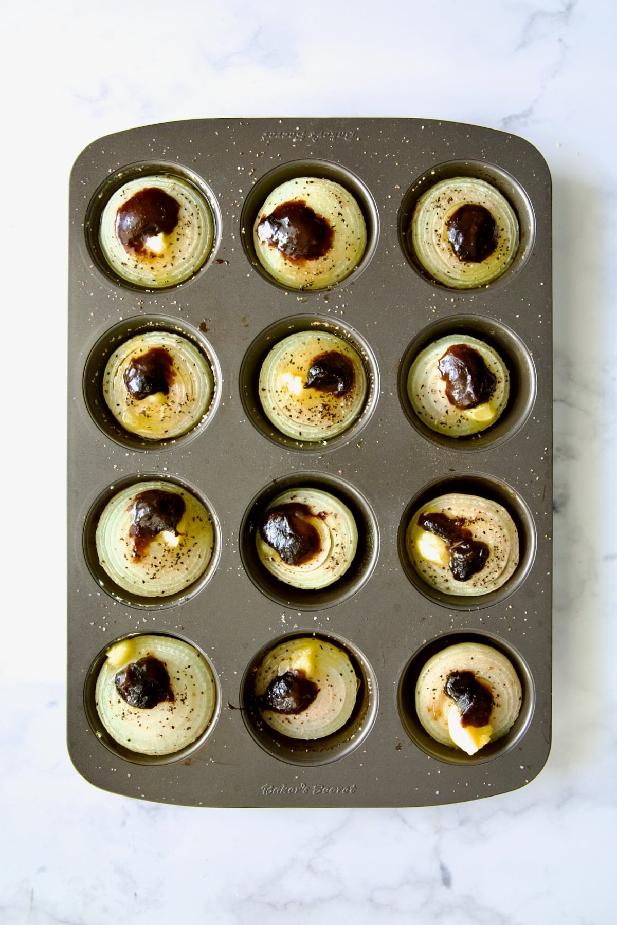 Onions halves in nonstick muffin pan topped with ghee and beef base concentrate.